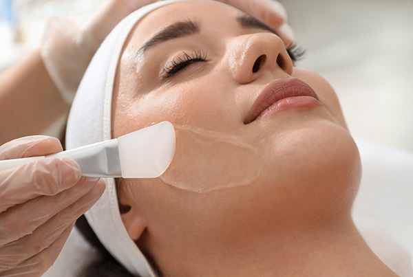 Applying a chemical peel treatment to a woman's face during a skincare session.