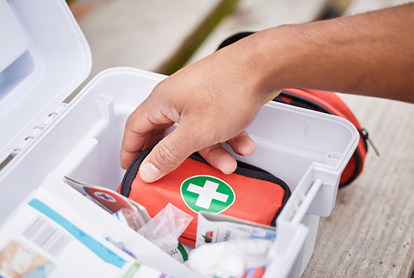 Hand reaching into a first aid kit with medical supplies visible.