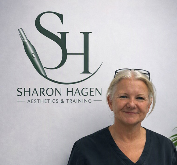 Sharon Hagen standing in front of her aesthetics and training logo backdrop