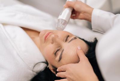 Woman receiving a facial treatment in a white robe with a skincare device.