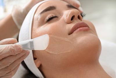 Applying a chemical peel treatment to a woman's face in a clinic setting.