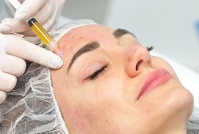Woman receiving a skin rejuvenation treatment with a syringe at an aesthetics clinic.